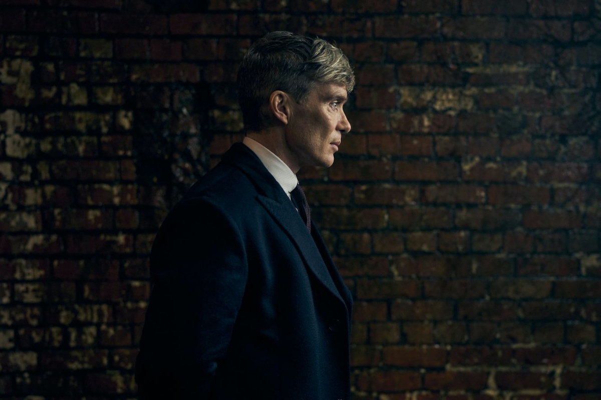 Cillian Murphy fekete téglafal előtt, profilból