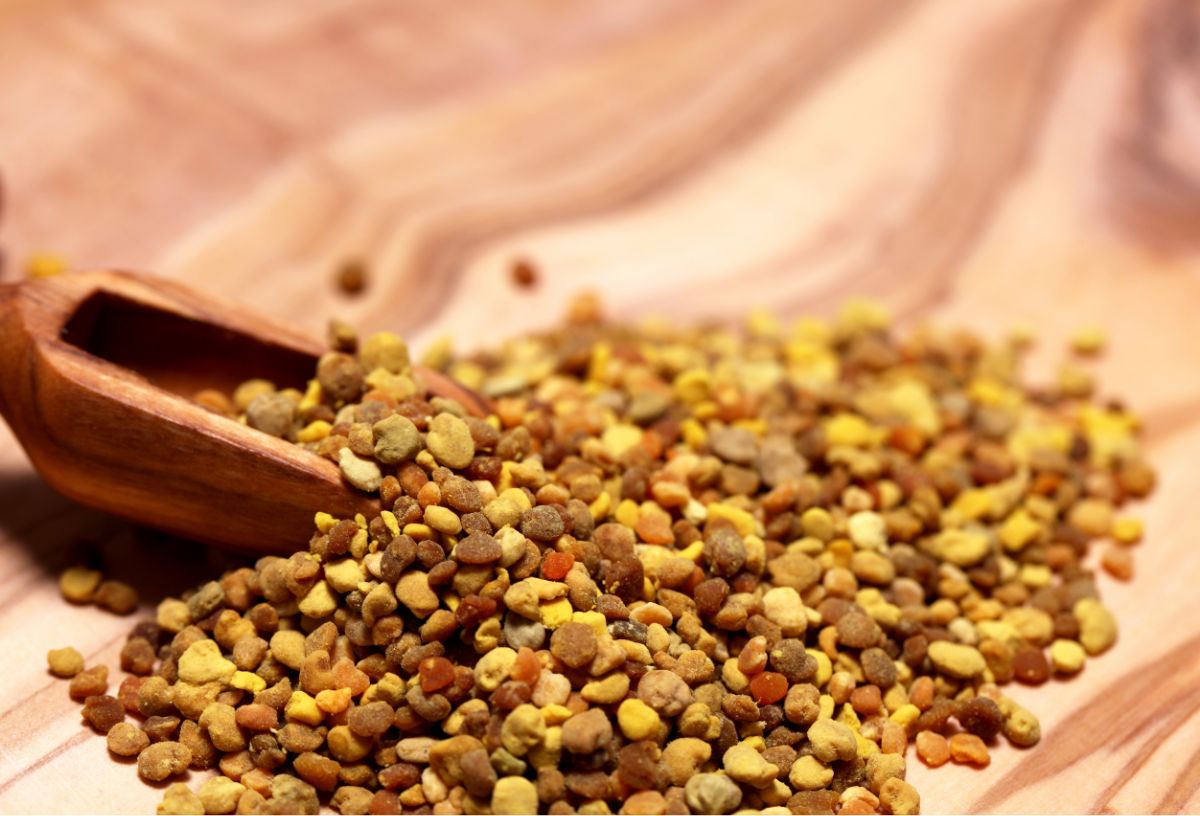 Méhpollen szemcsék fa asztalon, fa kiskanál nyúl bele a halomba