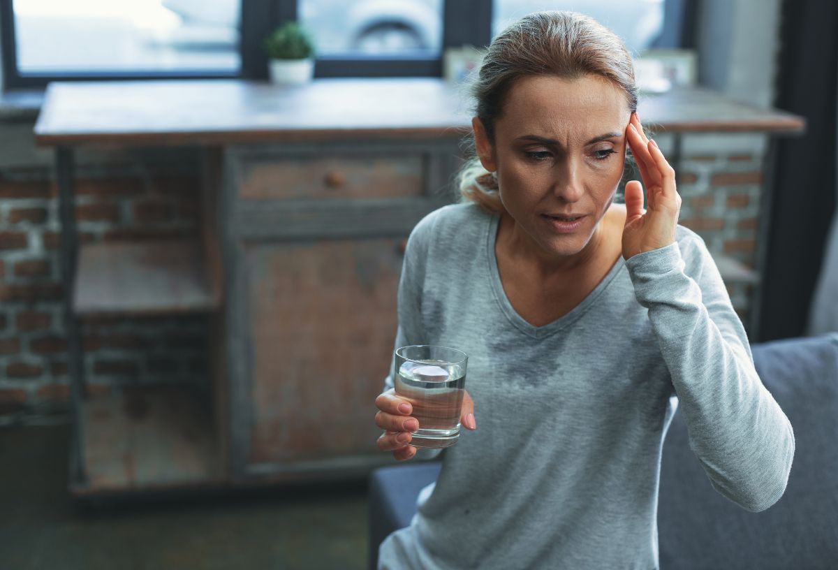 Ötvenes éveiben járó nő vizespohárral a kezében épp menopauza utáni hőhullámot él át