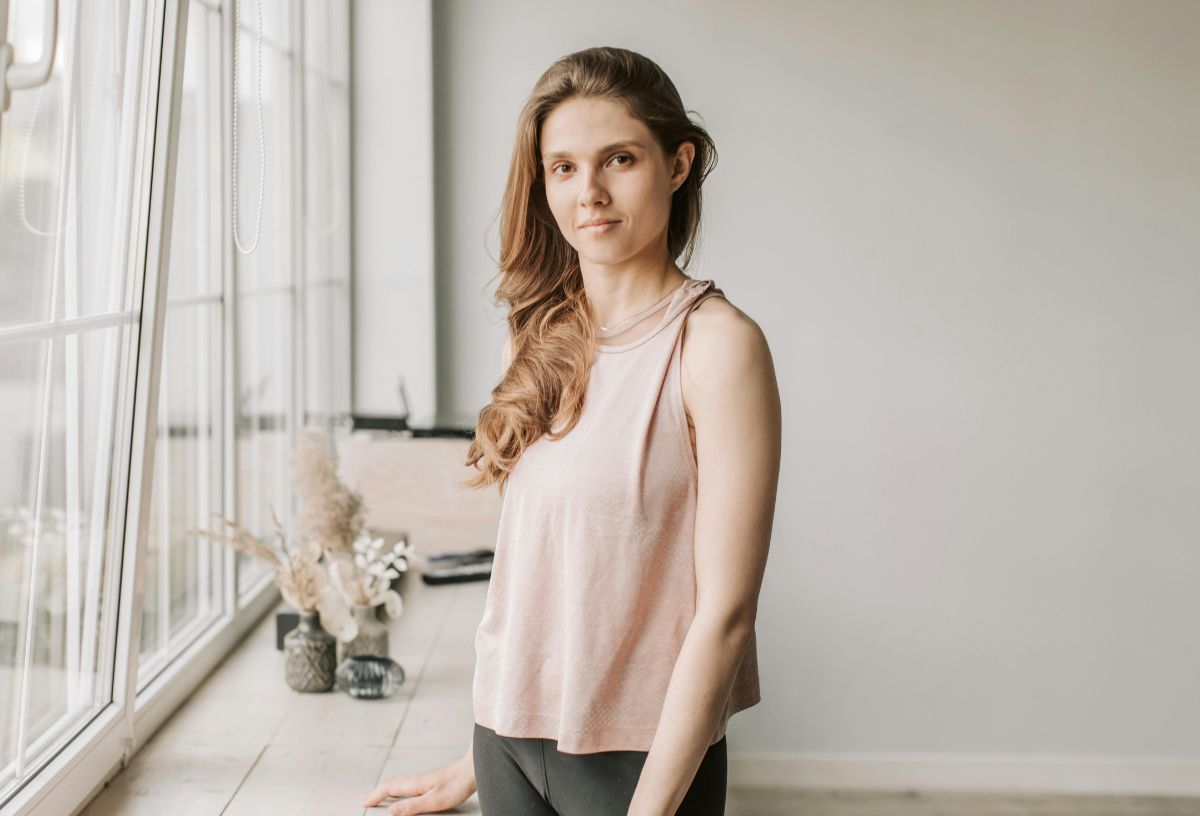 5 tipp, hogyan hozzuk helyre testbeszéddel a kapcsolatunkat vita után | Marie Claire Hosszú hajú nő egyenesen, nyitott testtartással áll ujjatlan felsőben ablakban