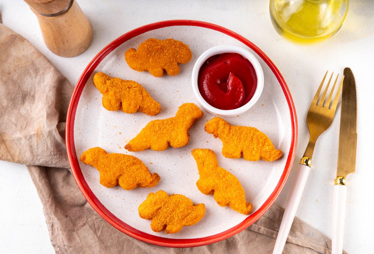 4 étel, amiben a legtöbb a mikroműanyag | Marie Claire Dinó alakú előre panírozott csirkefalatok fehér tányéron, mellette kis tálkában ketchup
