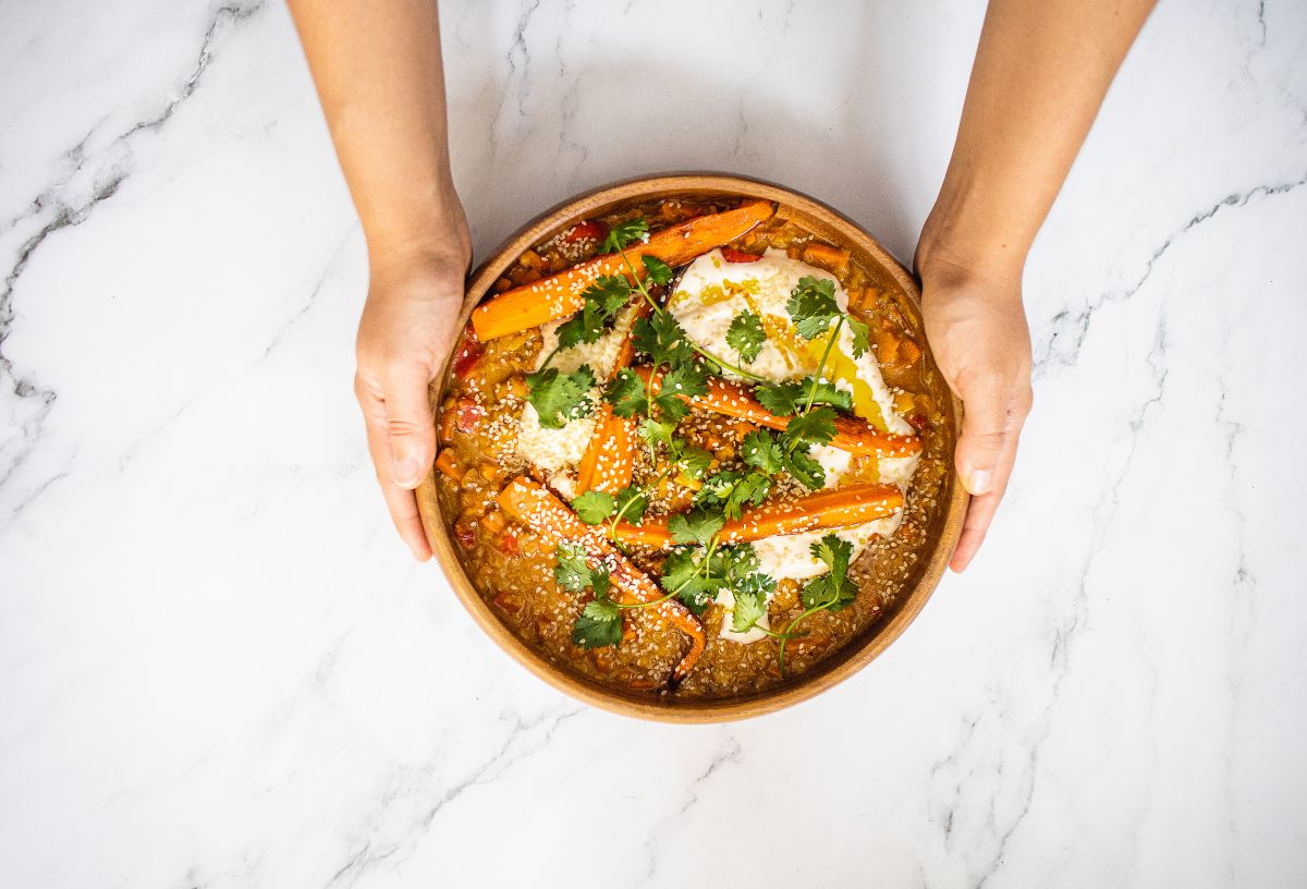 Női kéz márványasztalra tesz barna szószos vegán ételt