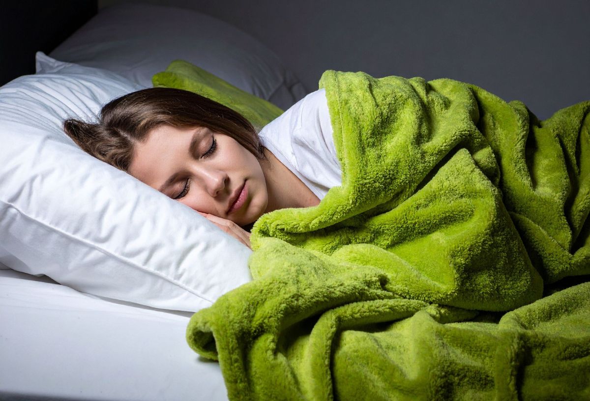 Nő zöld plédbe takarózva alszik fehér ágyneműn