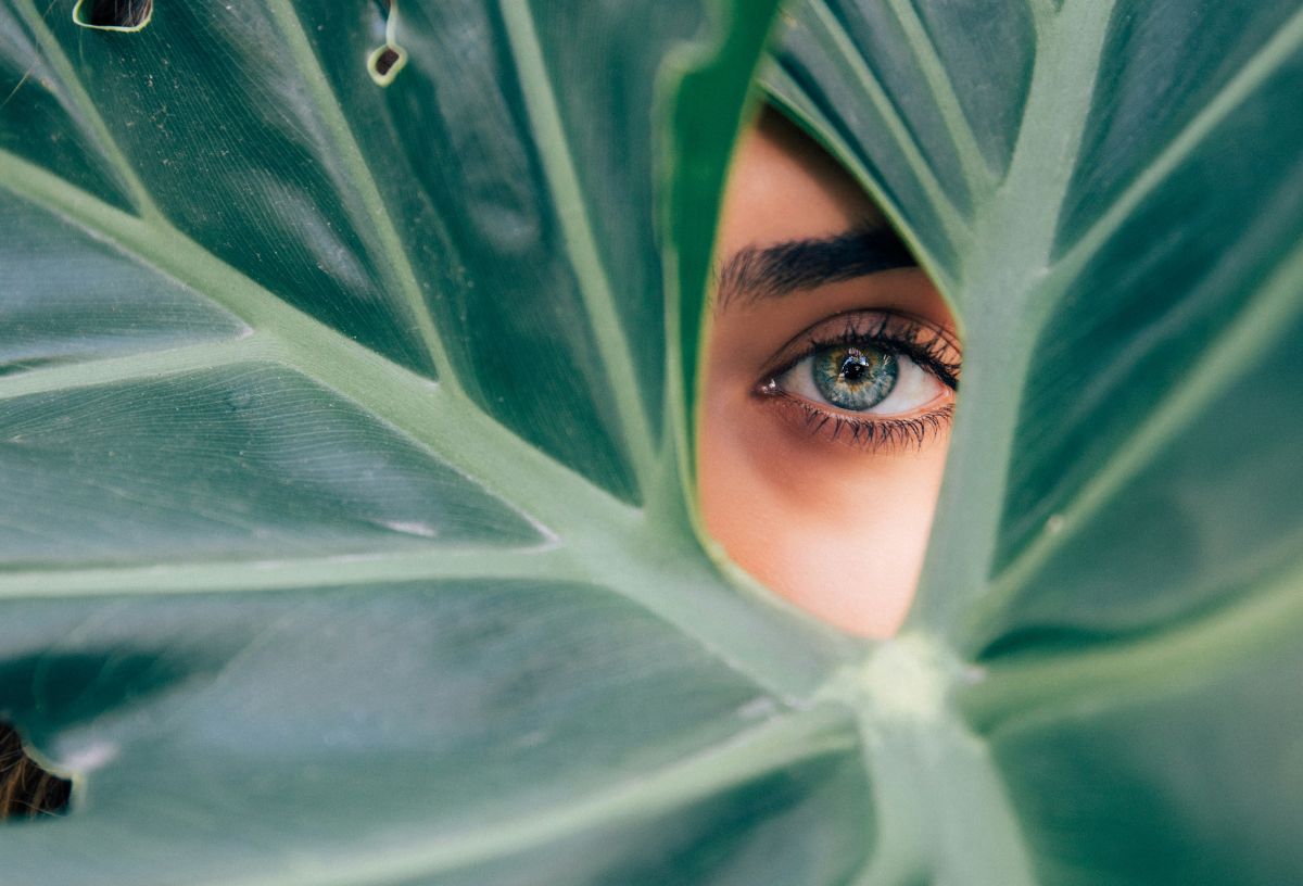 Kékeszöld szemű nő levélen keresztül néz ki