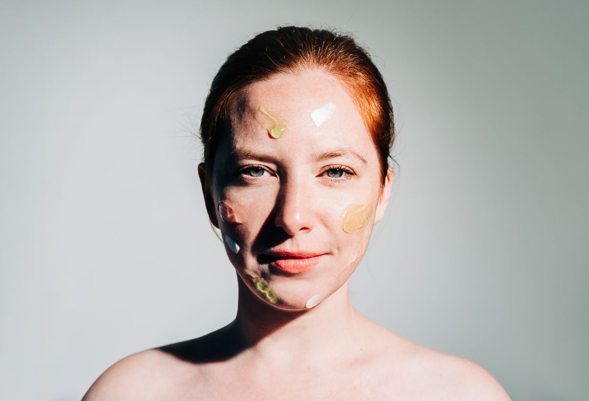 Nő kontrasztos fényben hátrakötött hajjal arcán különböző színű és állagú szérumokkal és krémekkel