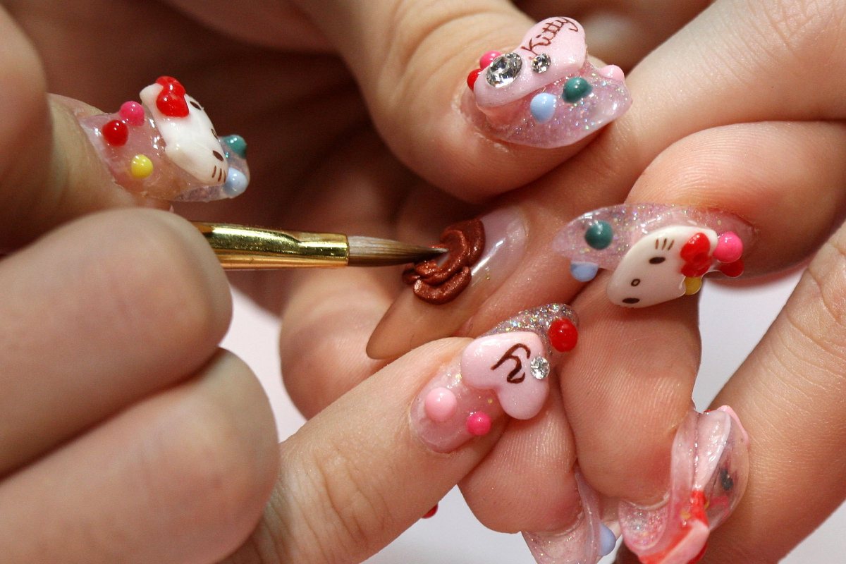 A manikűrös, akinek Hello Kitty mintás a körme, egy vendég körmén dolgozik