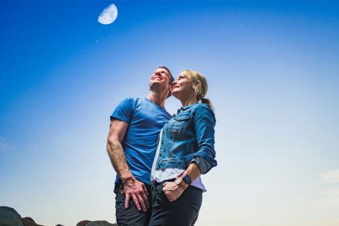 Szerelmes, ölelkező pár nézi az eget, a háttérben látszik a Hold