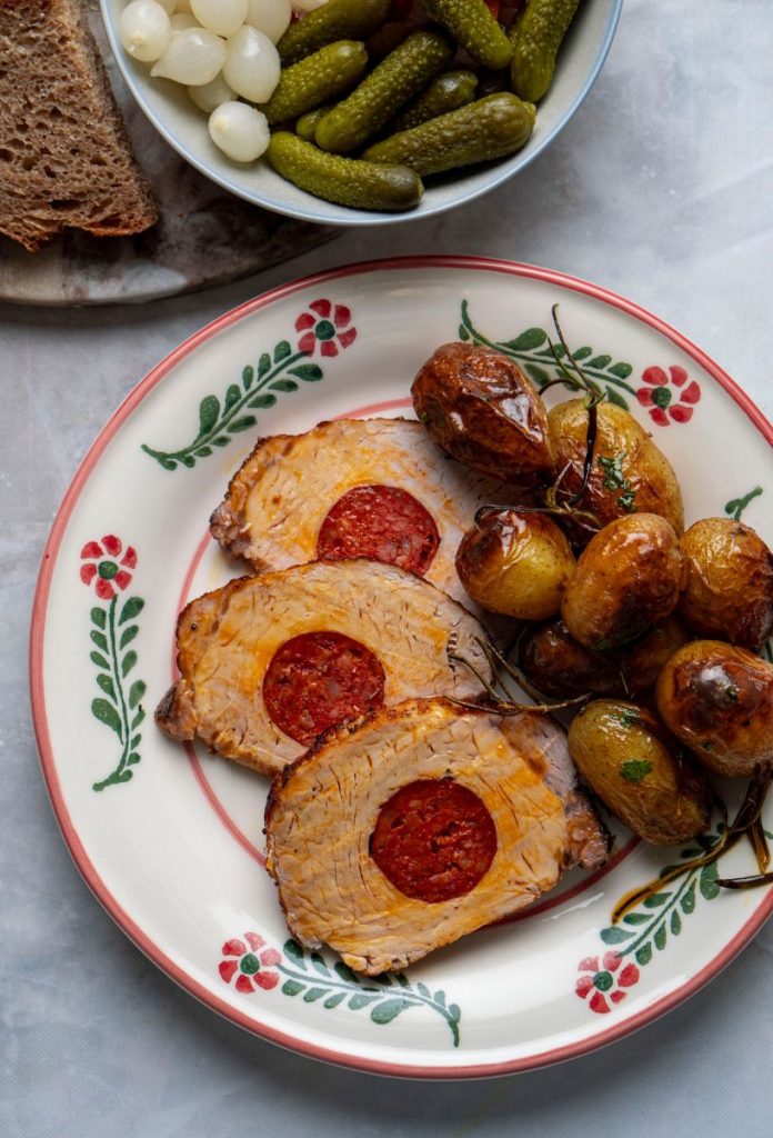 husveti-retro-menu-kolbasszal-toltott-karaj | Marie Claire Kolbásszal töltött karaj parázsburgonyával virágos tányéron, felette savanyúság