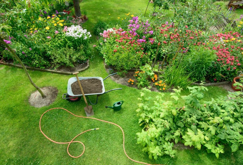 kullancs-kert-kialakitas | Marie Claire Gondozott kert felülnézetből, középen egy talicska virágföldel tele, mellette kerti slag