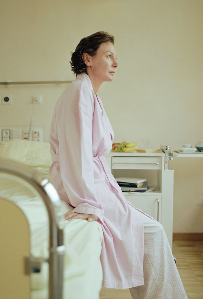 lynch-szindroma-rakkockazat-genetika | Marie Claire Nő rózsaszín köntösben kórházi ágy szélén ül