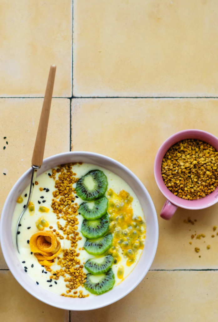 Csempézett pulton fehér tálban kivis-maracujás zabkása méhpollennel megszórva, mellette rózsaszín csészében méhpollen