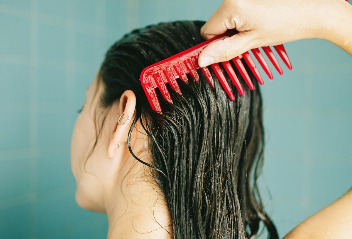 Micellás vízzel bekent zsíros haját fésüli nő piros nagyfogú fésűvel