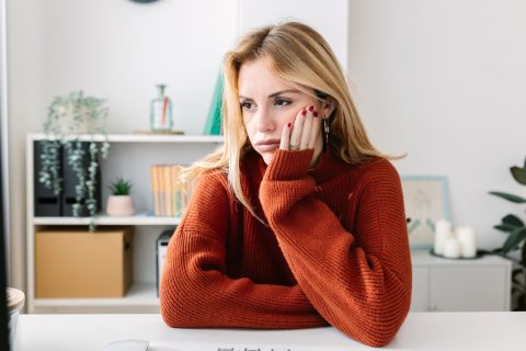 Egy szomorú fiatal nő néz maga elé, miközben könyököl és az egyik kezével az arcát fogja