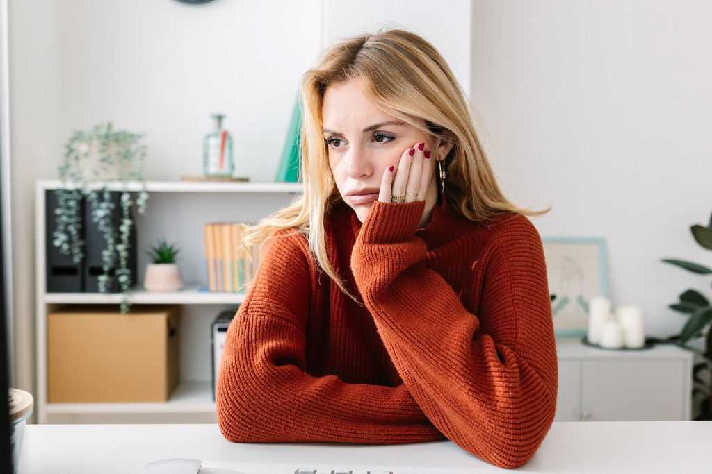 Egy szomorú fiatal nő néz maga elé, miközben könyököl és az egyik kezével az arcát fogja