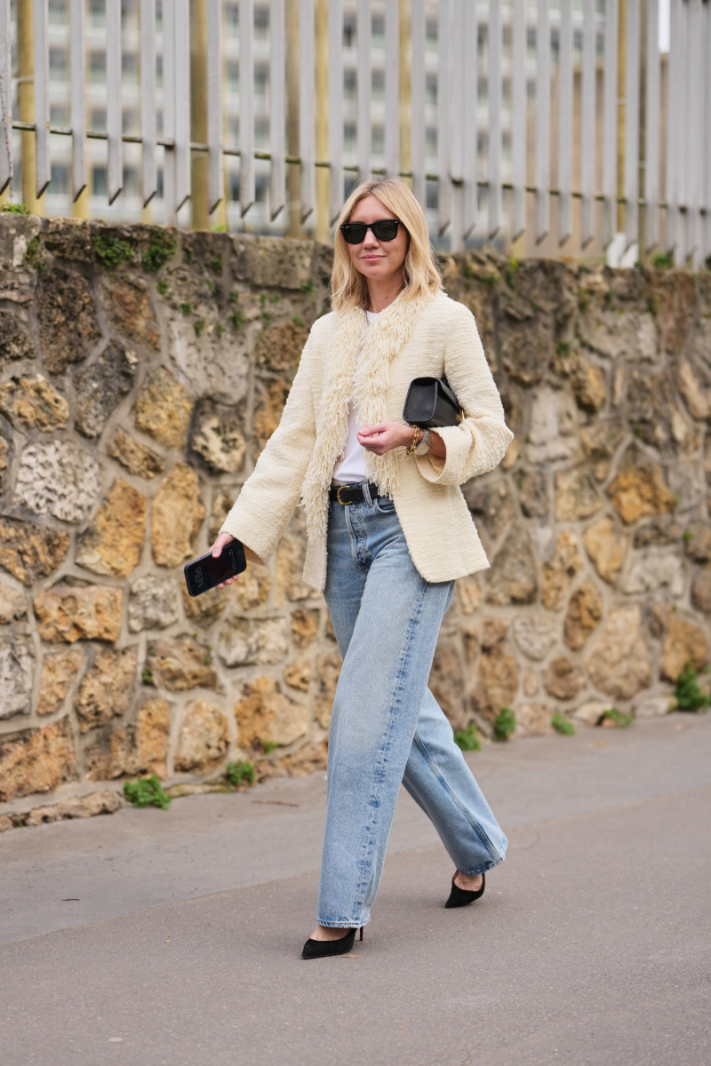 Lisa Aiken a 2026-os őszi–téli Rabanne show előtt: fekete napszemüvegben és egy krémszínű, rojtos gallérú tweed zakóban hódít, amit fehér pólóval és világoskék, egyenes szárú farmerrel tett lazává. A szettet egy fényes bőröv, egy elegáns kézitáska és egy hegyes orrú, fekete velúr magassarkú teszi teljessé.