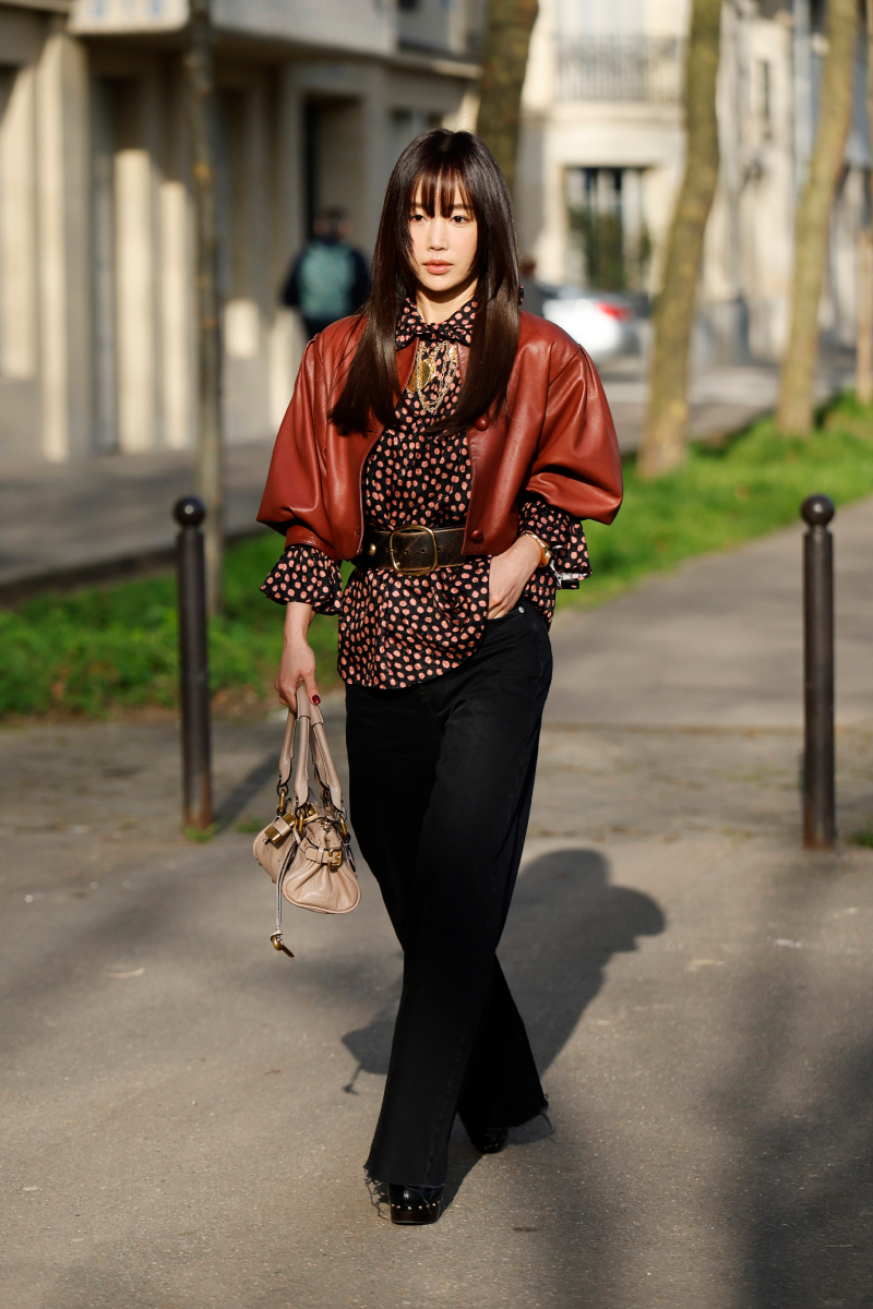 A Chloé 2026-os őszi-téli kapui előtt: ez a vendég fekete-rózsaszín blúzát barna, rövid ujjú bőrdzsekivel és övvel kombinálta. A fekete farmer mellé mi más is passzolna jobban, mint egy ikonikus, bézs Chloé táska?