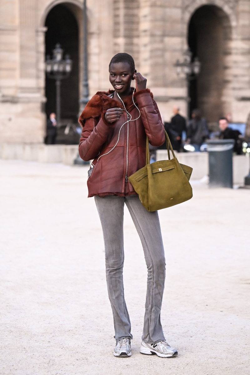 Rejoice Chuol modellt a Schiaparelli 2026-os őszi–téli show előtt kapták le ebben a piros dzsekiben, szürke skinny farmerben és fehér edzőcipőben. Zöld táskáját a karján viseli.