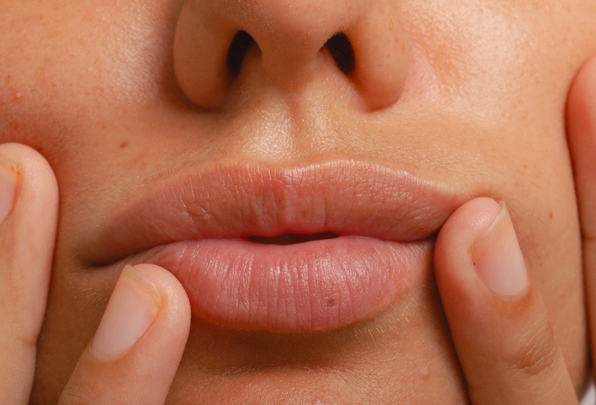 Közeli képen nő szája, enyhén csücsörít, két kezét a szája környékére rakja az arcán