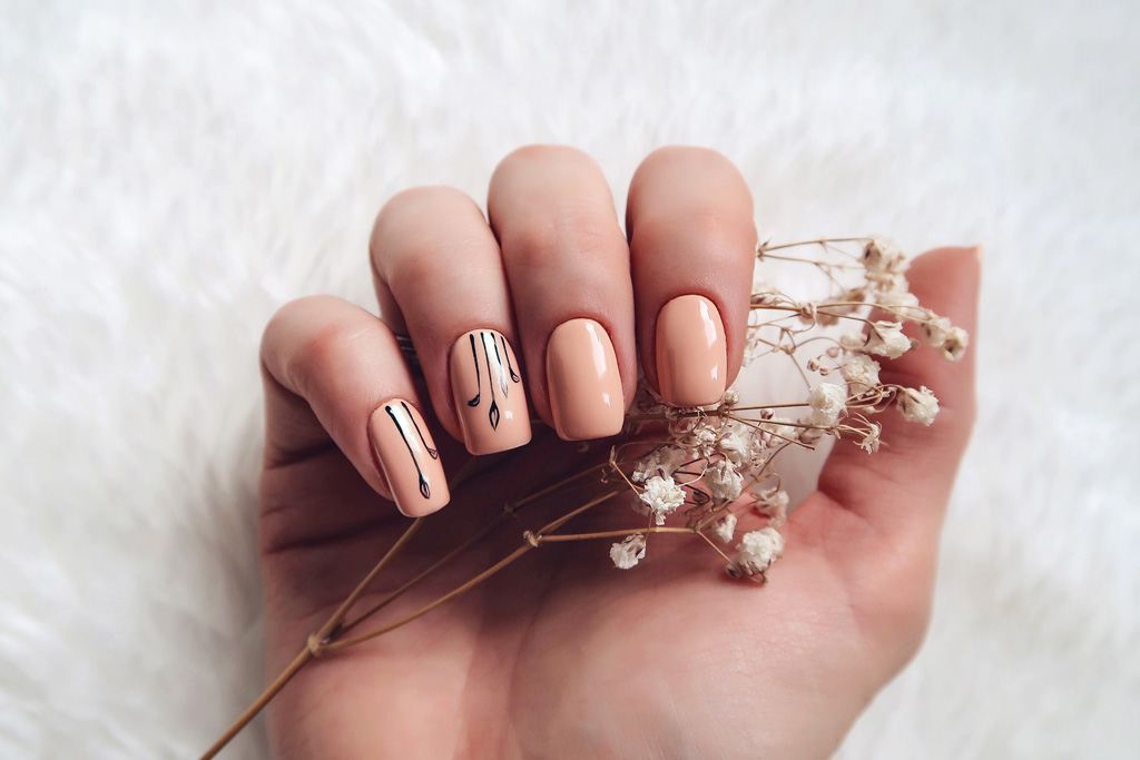 Egy női kéz, ami egy virágot tart a kezében, púderszínű körömlakk van a körmökön