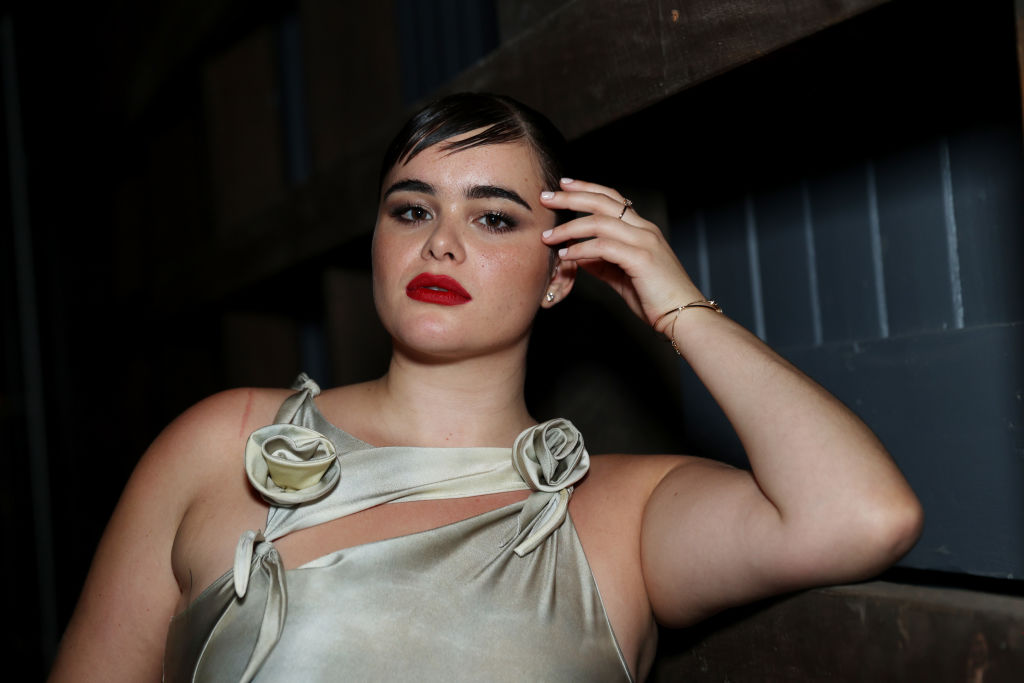 Barbie Ferreira rózsával díszített estélyi ruhában, piros rúzzsal a haját igazítja
