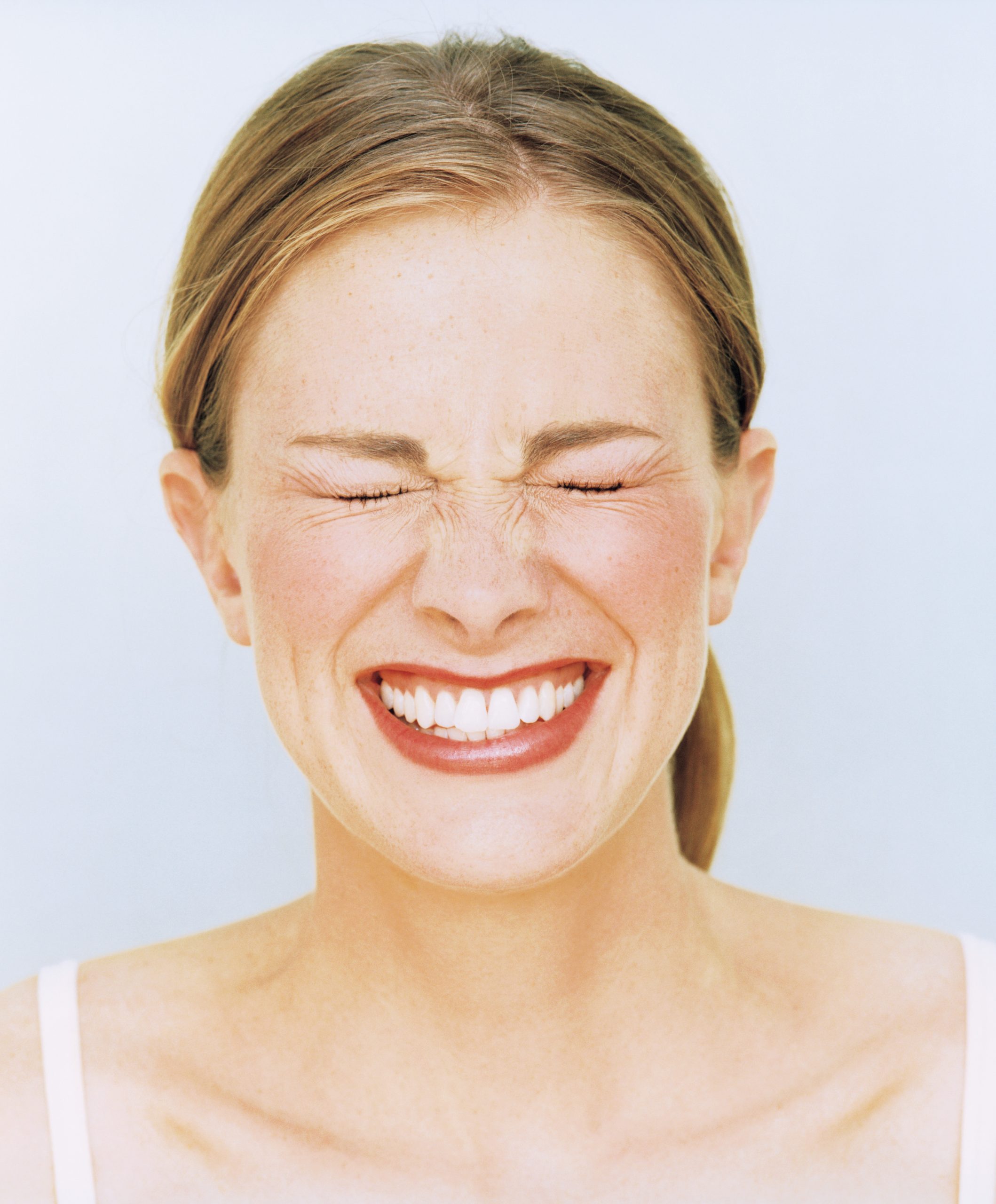 fiatal nő csukott szemmel nevet, fehér háttér előtt