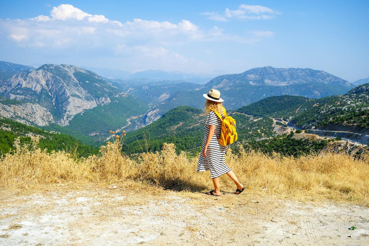 nő hegyek között kirándul kalapban és sárga hátizsákkal
