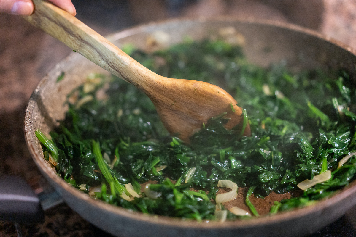 Spenót, fokhagyma és hagyma serpenyőben pirítva, vegetáriánus étel készítése, friss házi fogás.