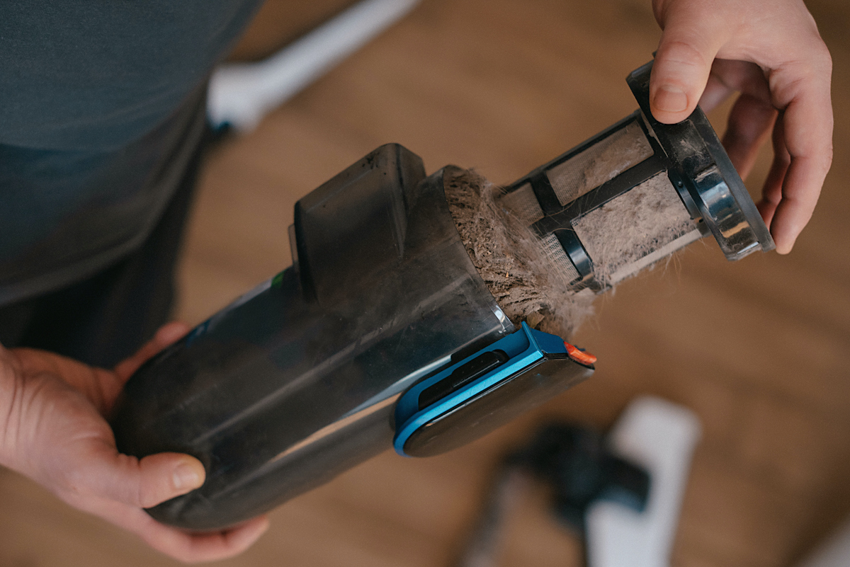 porszívó teli szűrőjét tartja egy férfi kéz