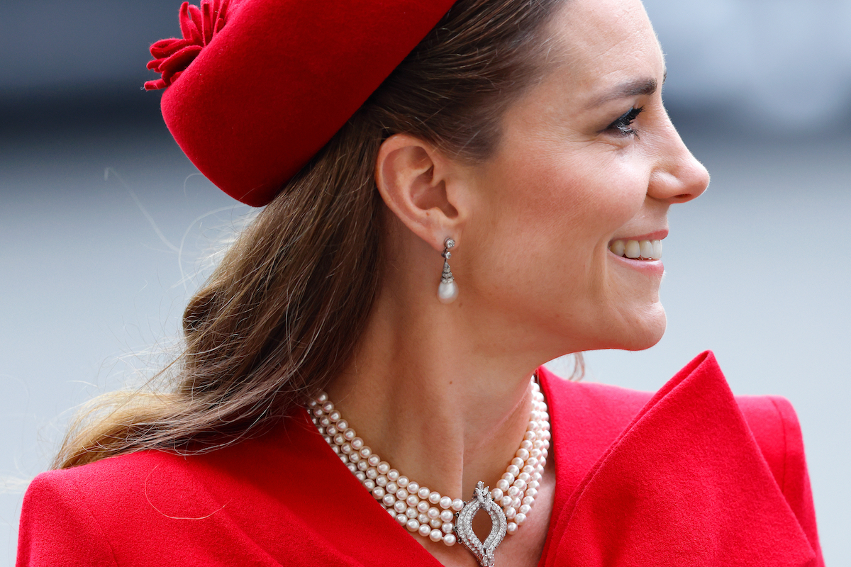 Katalin hercegné piros kalapban és ruhában, gyöngysorral és fülbevalóval, oldalra néz