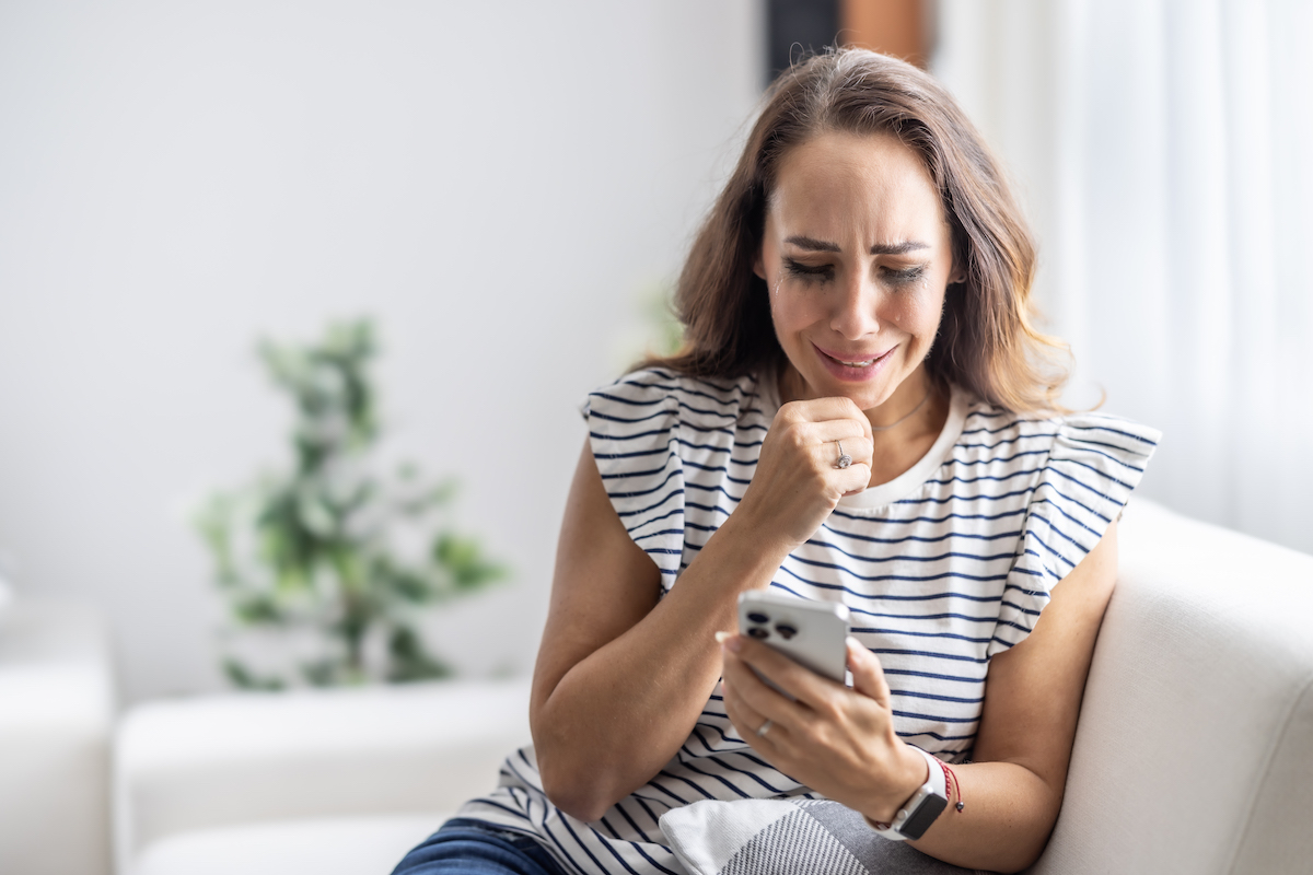 csíkos pólós nő sírva nézi a telefonját