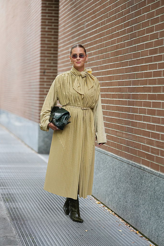 Egy nő az utcán sárga kabátban, masnival a nyakán