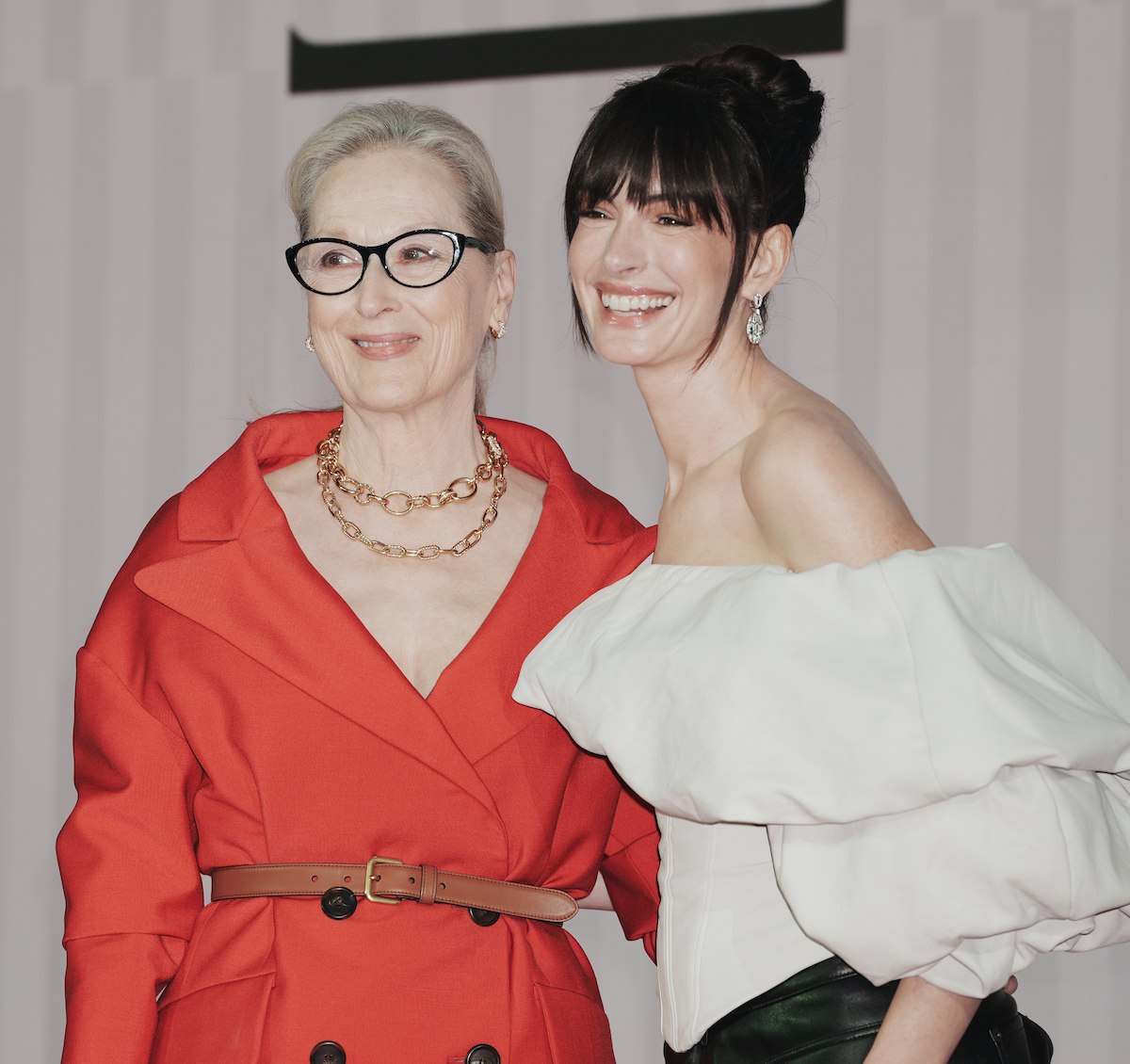 Meryl Streep piros ruhában övvel és Anne Hathaway fehér fodros blúzban mosolyog