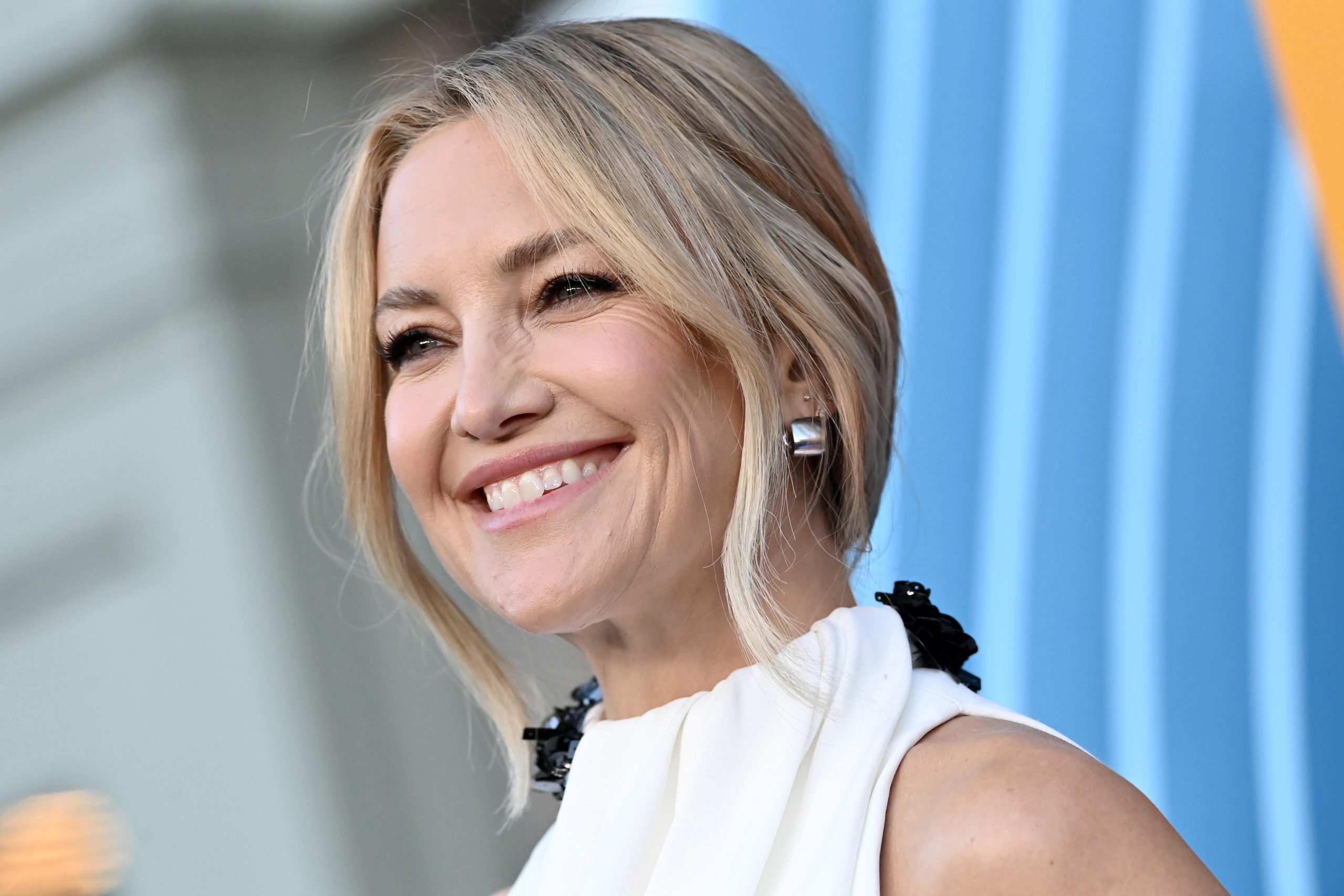 Kate Hudson szőke, copfba kötött hajjal kék háttér előtt