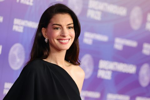 Anne Hathaway félvállas fekete ruhában, lila háttér előtt