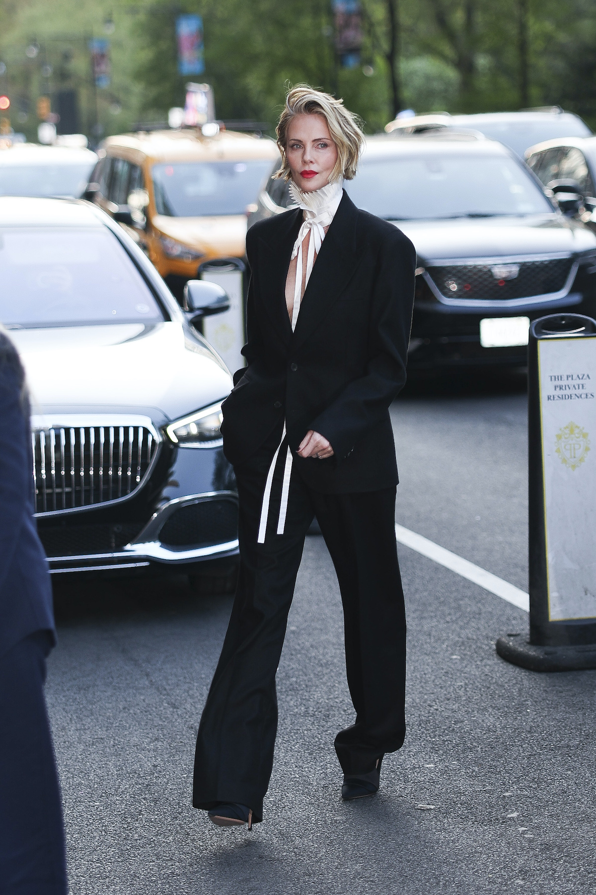 Charlize Theron fekete kosztümben autók között sétál