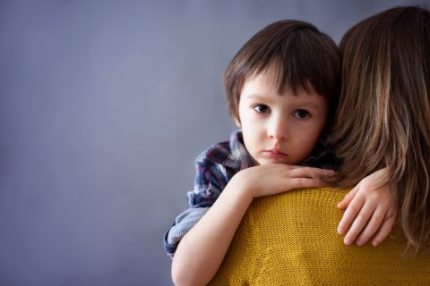 Szomorú kisgyerek, fiú, aki otthon átöleli az anyját