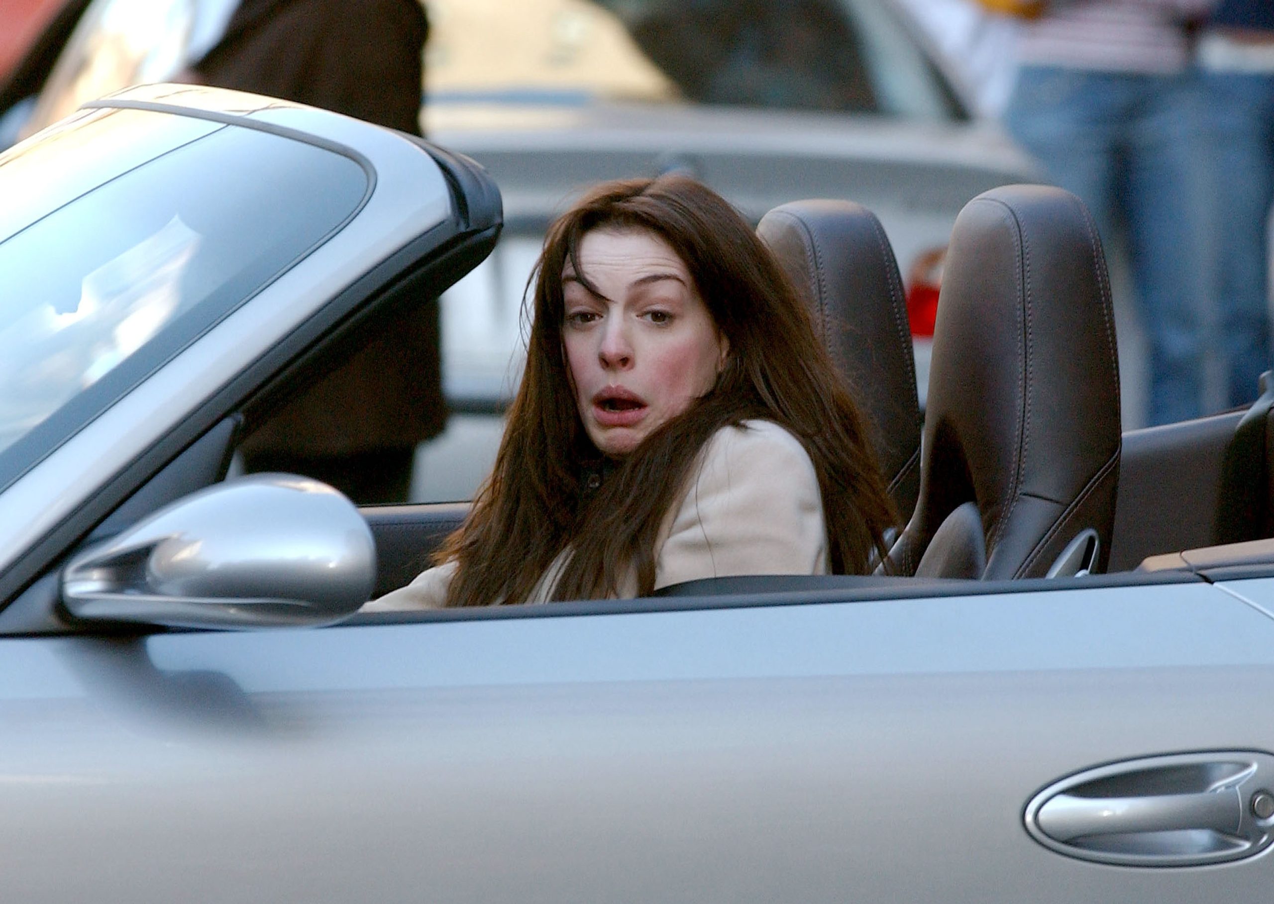 Anne Hathaway behúzott nyakkal, ijedten ül egy nyitott tetejű autóban