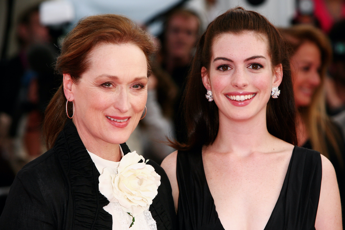 Meryl Streep fekete blézerben és fehér virágdíszítéses blúzban, és mellette Anne Hathaway fekete ruhában