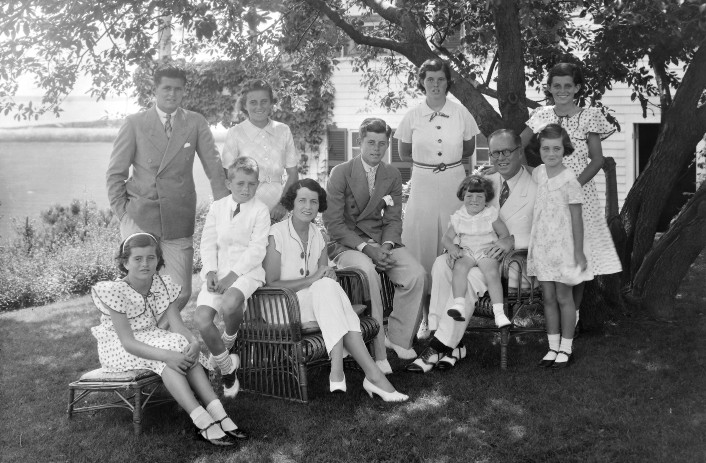 A Kennedy család portréja, amint fák árnyékában ülnek, Hyannisban, Massachusettsben az 1930-as években. Balról jobbra ülnek: Patricia Kennedy, Robert Kennedy, Rose Kennedy, John F Kennedy, idősebb Joseph P Kennedy, ölében Edward Kennedy, balról jobbra állnak: ifjabb Joseph P Kennedy, Kathleen Kennedy, Rosemary Kennedy, Eunice Kennedy (hátul, pöttyös mintával) és Jean Kennedy.