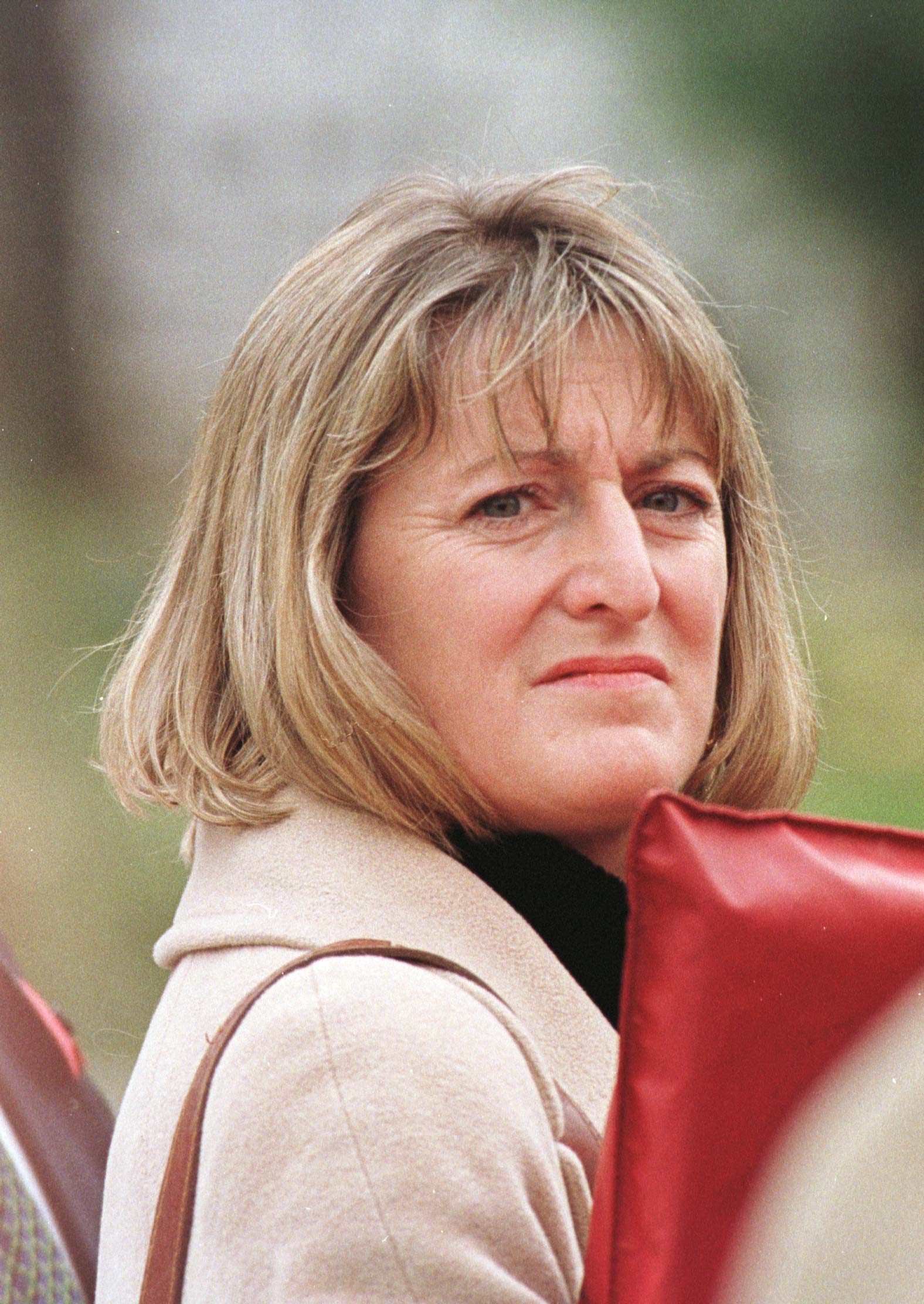 Sandy Henney állig érő szőke hajjal, piros táskát tart arca elé