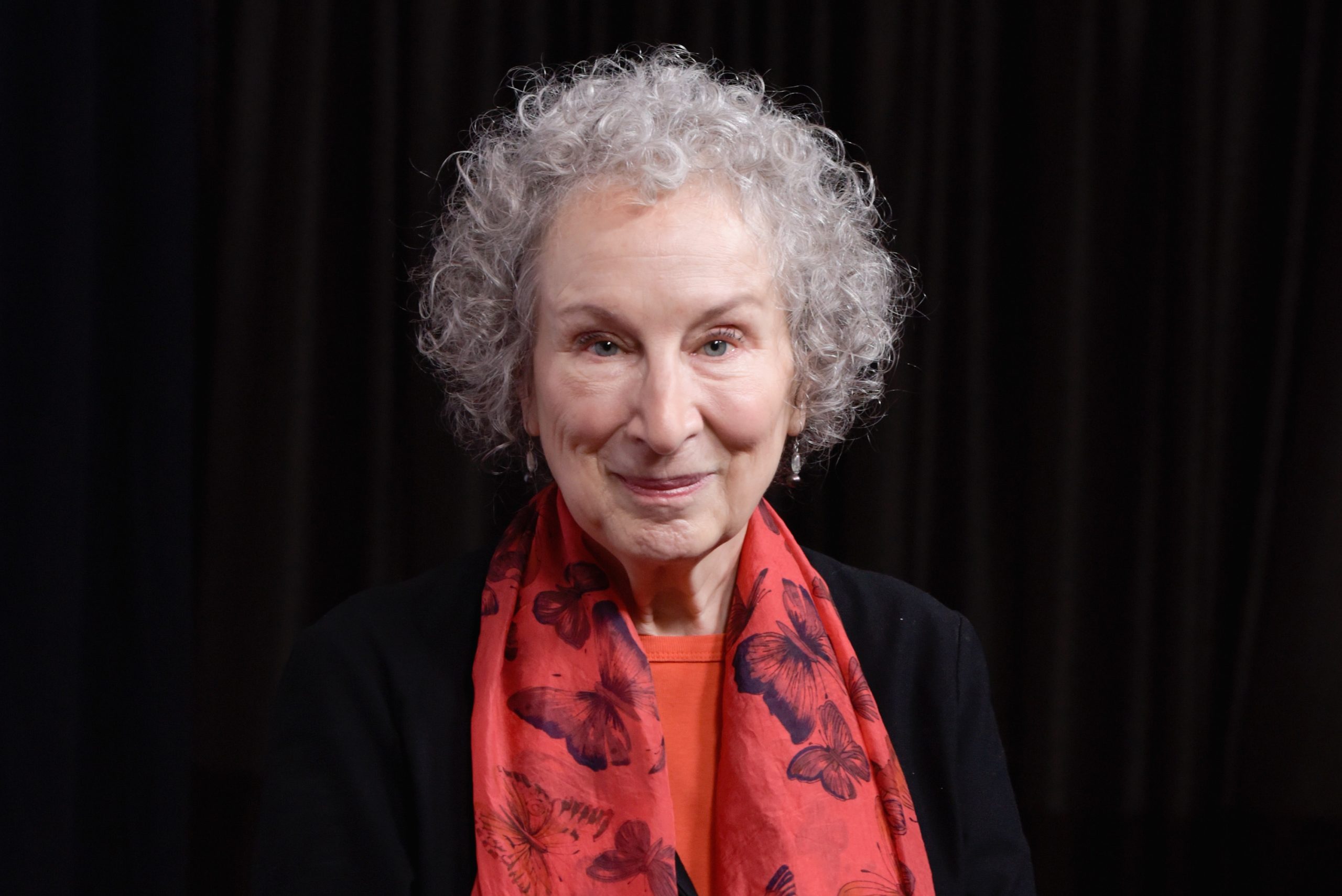Margaret Atwood piros sállal a nyakában, fekete háttérrel