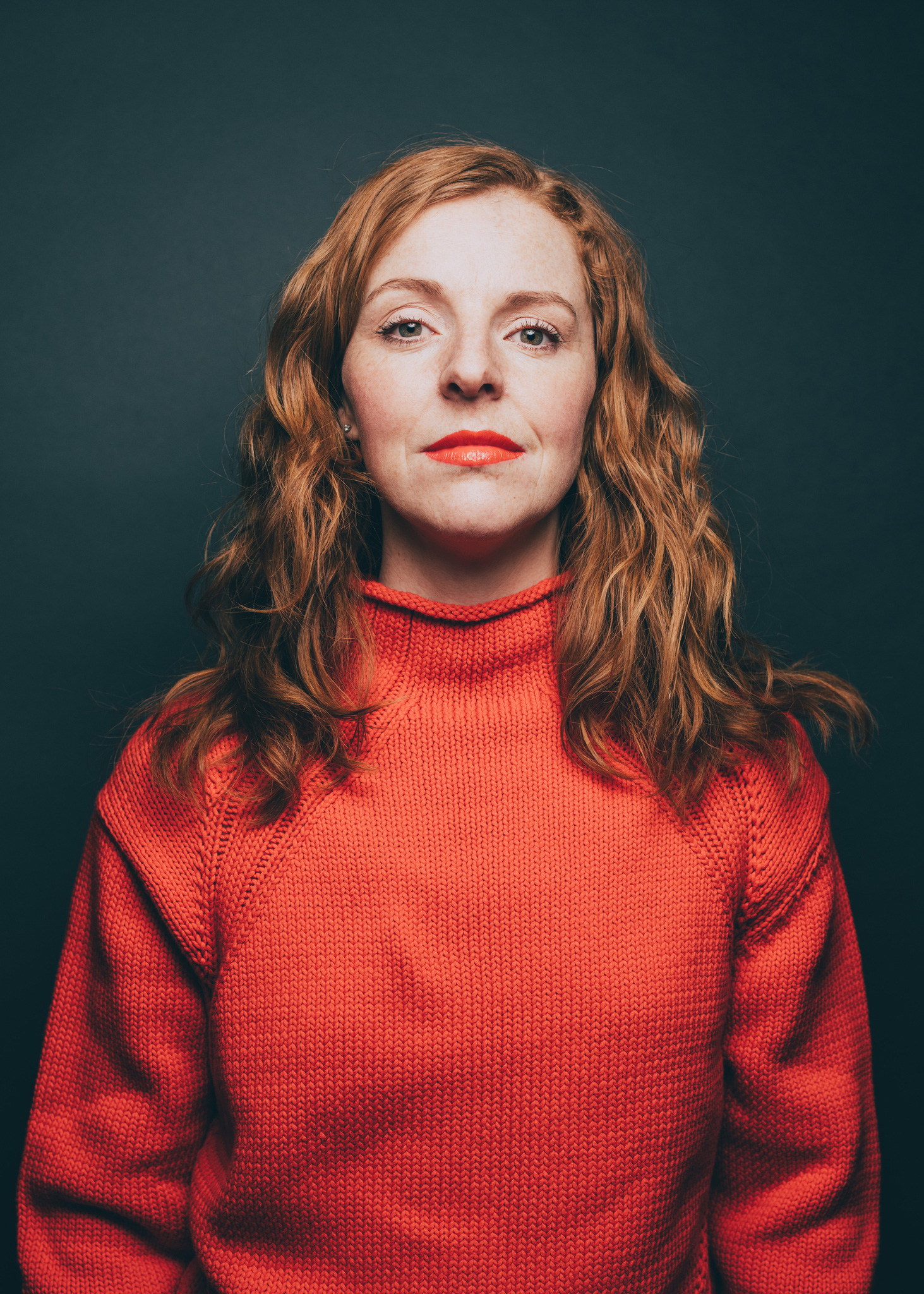 Egy vörös hajú, narancssárga pulóvert viselő nő arrogánsan néz előre