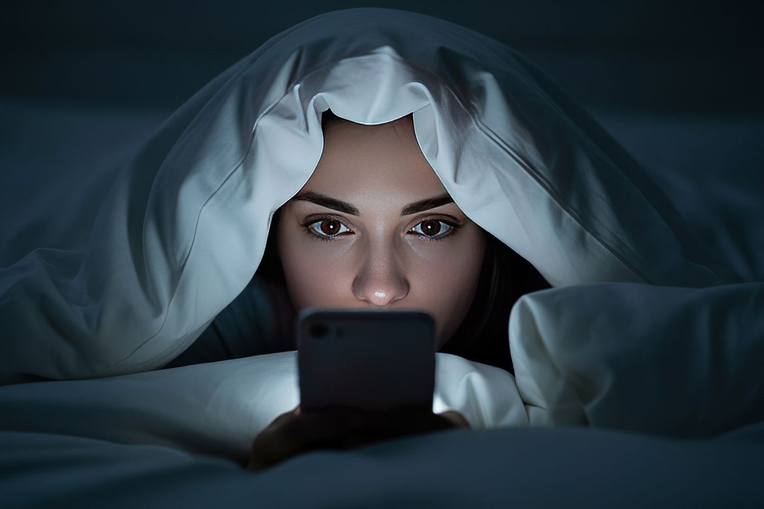 Nő takaró alatt ágyban okostelefonozik