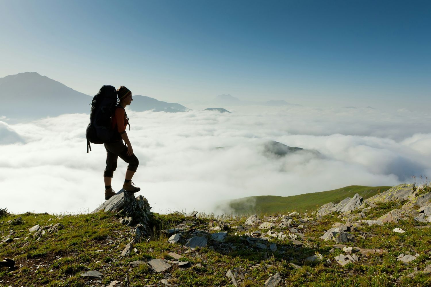 Túrázó nő sziluettje hegy tetején, körülötte felhők az orom körül