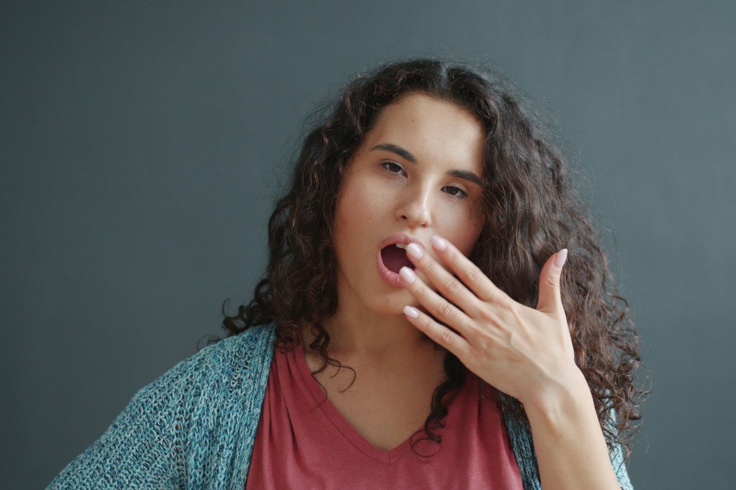 Barna, hullámos hajú nő kardigánban és pólóban kitátott szája elé teszi a kezét, zöld háttér