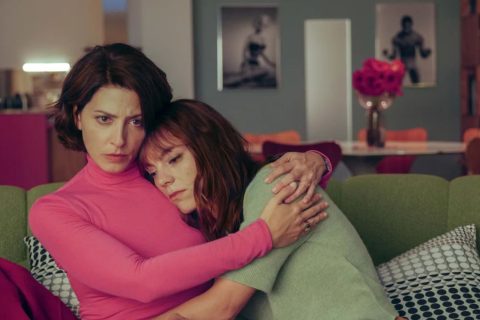 Cannes 2026 filmpremierek, jelenet a Bitter Christmas című filmből, két nő átöleli egymást kanapén ülve, egyik rózsaszín, másik zöld felsőben