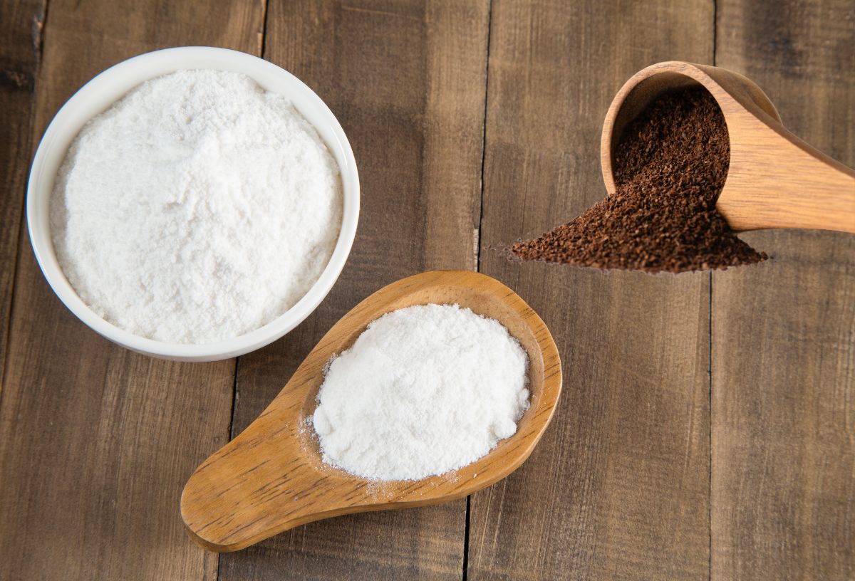 Szódabikarbóna fehér kerámatálban és fa kiskanálban, mellette kávézacc fa kanálból ömlik ki, fa háttér