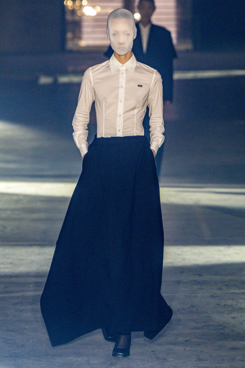 Vetements 2026. tavasz–nyár bemutatón vonuló modell fátyollal az arcán, fehér ingben, fekete szoknyában