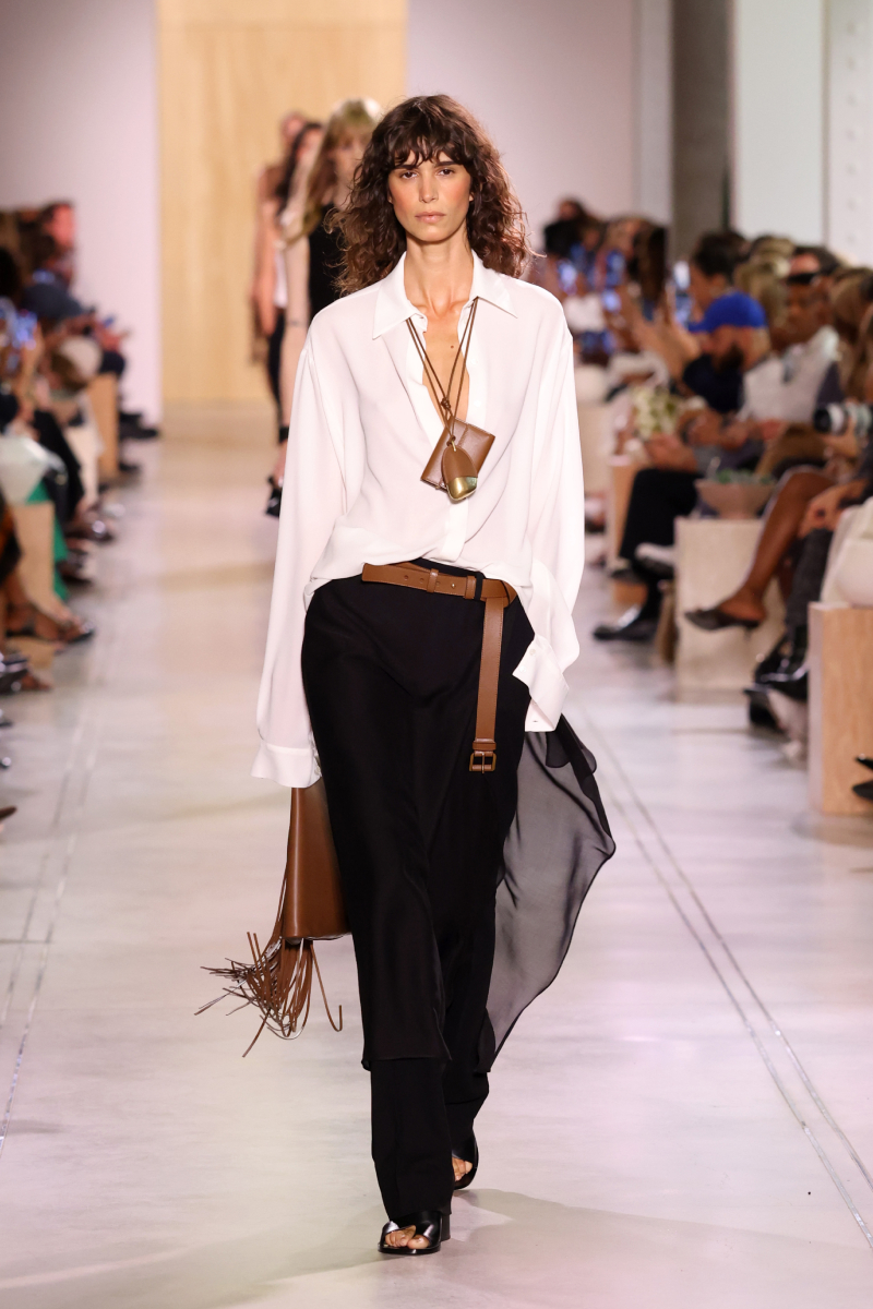 Michael Kors 2026. tavasz–nyár bemutatón barna hajú modell vonul fehér ingben, fekete nadrágban
