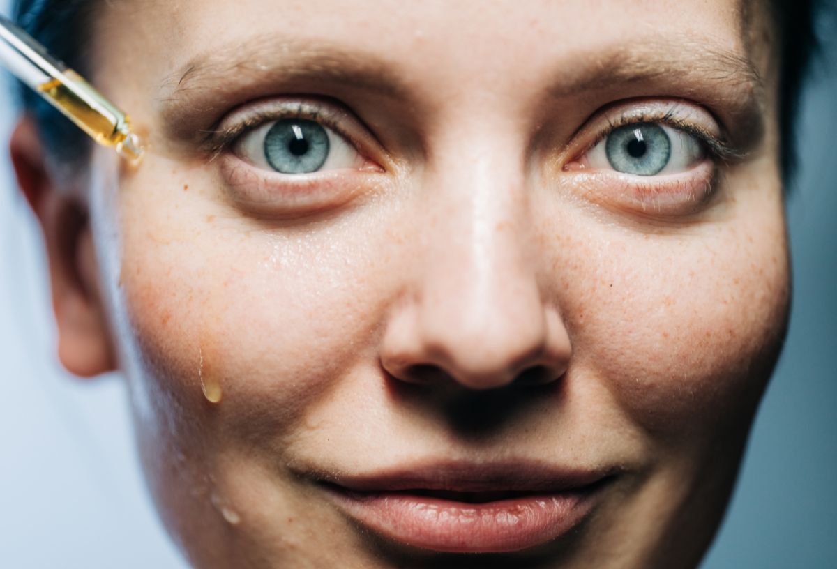 Kék szemű nő közeli képen mandulasav szérumot csepegtet az arcára